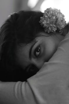 a black and white photo of a woman with flowers in her hair laying on the bed