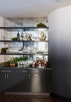 a kitchen filled with lots of bottles and glasses on top of a metal shelf next to a sink