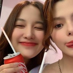 two young women are posing for the camera with coca - cola cans in their hands