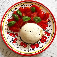 a plate with tomatoes, mozzarella and basil leaves on the side sitting on a wooden table