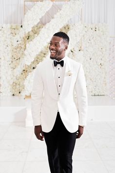 a man in a white tuxedo smiles at the camera while wearing a black bow tie