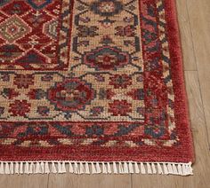 a red rug with fringes on the floor in front of a wooden flooring area