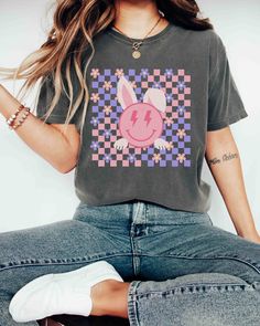 "A Comfort Colors unisex \"CHECKERED SMILEY BUNNY\" garment-dyed t-shirt made 100% with ring-spun cotton.  Retro Easter Vibes Shirt, Happy Easter Day TShirt, Smiley Bunny Tee, Hip Hop, Hunny Bunny Easter Shirt For Woman, Bunny Lover Teacher Gift  For an Oversized Look order 1 to 2 sizes larger than your normal size. 🌟100% ring-spun cotton 🌟Heavy fabric (6.1 oz/yd² (206.8 g/m 🌟Relaxed fit RETURNS: All products are made-to-order and because of the nature of these items, all sales are final unle Cute Graphic Design Tops For Spring, Cute Graphic Design T-shirt For Spring, Fun Graphic Design Tops For Spring, Fun Spring Graphic Design Tops, Funny Screen Print Tops For Spring, Funny Print Tops For Spring, Funny Spring Shirt With Screen Print, Funny Screen Print Shirt For Spring, Easter Vibes