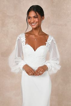 a woman wearing a white wedding dress with sheer sleeves and an open back, smiling at the camera