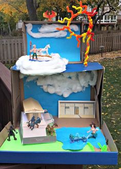 an open cardboard box with toys in it on top of a blue table outside near a fence