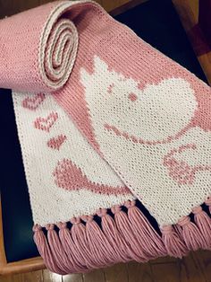 a pink and white knitted blanket sitting on top of a wooden table