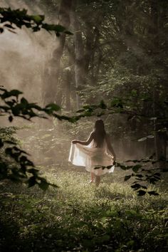 a woman in a white dress is walking through the woods