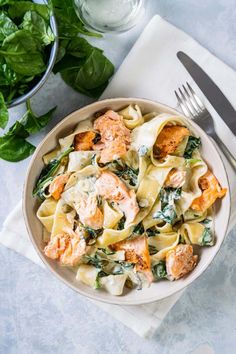 a bowl of pasta with salmon and spinach on a napkin next to silverware