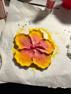 a yellow flower sitting on top of a piece of paper next to paint and brushes