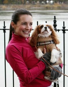 a woman holding a dog in her arms near a fence with water and trees in the background