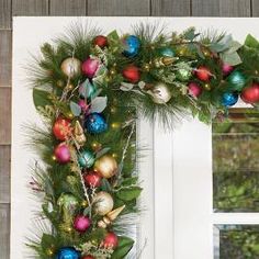 a wreath decorated with ornaments and greenery on a window sill in front of a white door