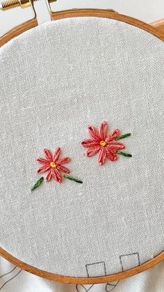 two red flowers are sitting on top of a piece of white fabric in front of a wooden hoop