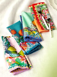 four colorful napkins with forks on them sitting on a white tablecloth next to each other