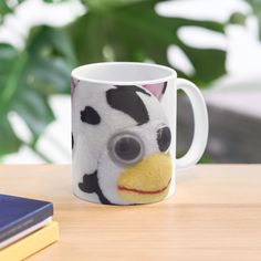 a coffee mug with a face painted on it sitting on a table next to a book