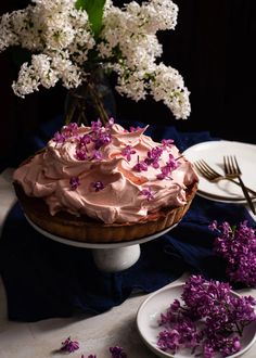 a cake with pink frosting sitting on a table next to purple flowers and plates