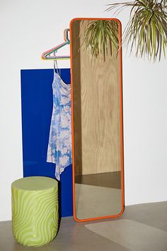 a mirror sitting on top of a table next to a green stool and potted plant