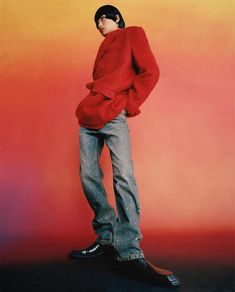 a man standing in front of an orange and pink background with his hands on his hips