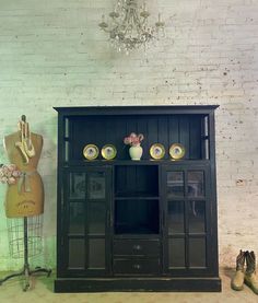 an old fashioned black cabinet next to a mannequin and vase with flowers on it