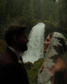 the bride and groom are looking at each other in front of a waterfall on their wedding day