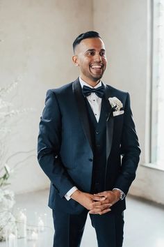 a man in a tuxedo smiles as he stands next to a flower arrangement