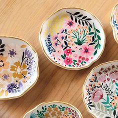 four colorful floral plates sitting on top of a wooden table