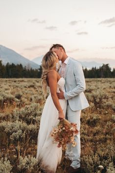 a bride and groom kissing in the middle of a field with mountains in the background