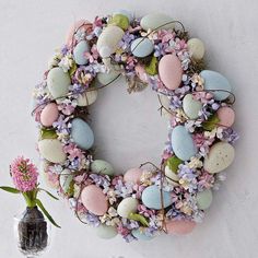 a wreath made out of eggs and flowers next to a vase with a flower in it