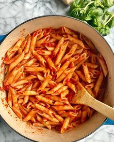 a pot filled with pasta and sauce on top of a marble counter next to vegetables