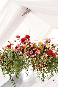 an arrangement of flowers hanging from the ceiling in front of a white tented area