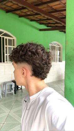 a young man with curly hair standing in front of a green wall and looking off into the distance