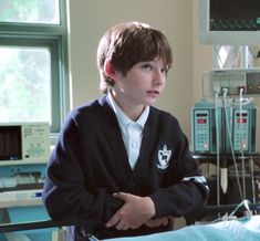 a young boy sitting in a hospital bed with his arms crossed and looking off to the side