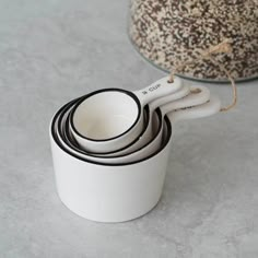 four white cups with black handles are stacked on top of each other in front of a bowl