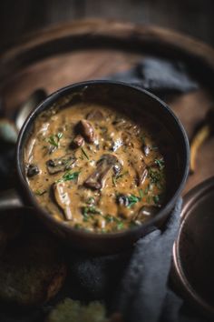 a bowl filled with mushroom soup on top of a wooden table next to some bread