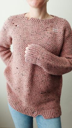 a woman wearing a pink sweater with holes in the front and back, standing against a white wall