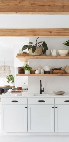 a white kitchen with open shelving and potted plants