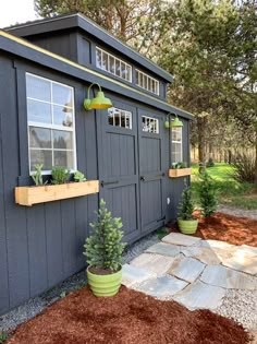 a small shed with two plants in the window and some dirt on the ground next to it