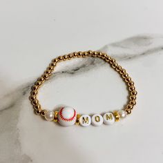 a gold beaded bracelet with the word mom written on it and a baseball ball