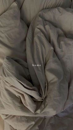 an unmade bed with the word home written on it's pillow and comforter