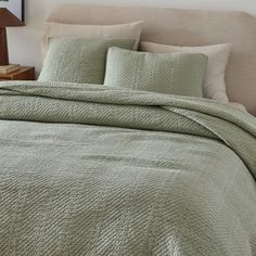 a bed with green bedspread and pillows on top of it, next to a night stand