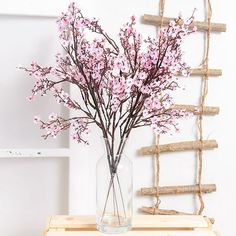 a vase filled with pink flowers sitting on top of a wooden table next to a ladder