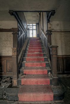 an old staircase with red steps leading up to a window in the middle of it