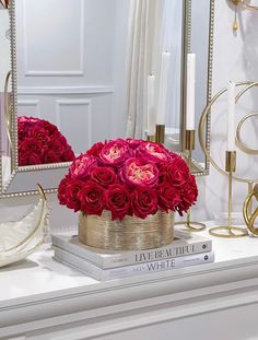 a white mantle topped with a vase filled with red roses and candles next to a mirror