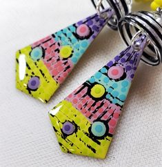 two colorful earrings are hanging from a keychain on a white surface with yellow beads