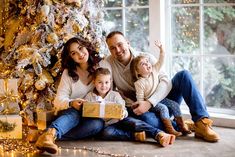 a family sitting in front of a christmas tree holding a gift box and smiling at the camera