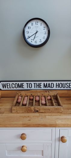 a clock on the wall above a wooden crate with eggs in it and a sign that says welcome to the mad house