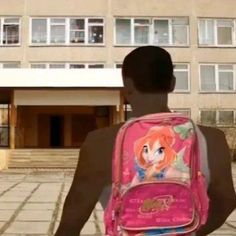 a young man with a pink backpack in front of a building and another person walking towards it