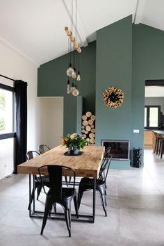 a dining room with green walls and wooden table surrounded by black chairs in front of a fireplace