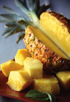 a pineapple and sliced pineapple on a red plate with minty garnish