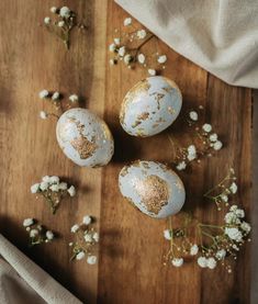 three decorated eggs sitting on top of a wooden table next to baby's breath flowers