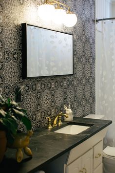 a bathroom with black and white wallpaper, gold faucets and a mirror above the sink